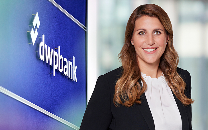 Zu sehen ist Kristina Lindenbaum, Vorständin der dwpbank. Sie hat lange braune Haare und ein offenes Lächeln. Neben ihr steht auf einer blauen Wand der Schriftzug dwpbank.