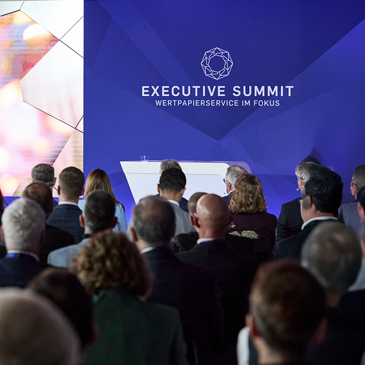 Ein Foto vom Executive Summit 2025 der dwpbank: Das Publikum schaut auf eine große Bühne mit blauer Leinwand.