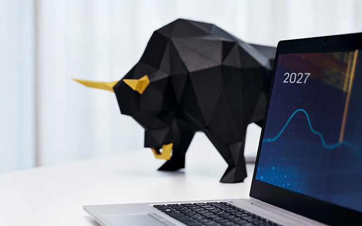 Ein geöffneter Laptop im Vordergrund zeigt ein Börsen-Chart mit der Jahreszahl 2027, während im unscharfen Hintergrund eine moderne, geometrische Skulptur eines schwarzen Bullen mit goldenen Hörnern steht – passend zur Branchenumfrage "AVD-Barometer 2027" von dwpbank und lemon.markets, die Finanzinstitute über die Einführung des Altersvorsorgedepots befragte.